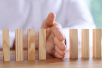 Photo of Risk. Man stopping domino effect at wooden table, closeup