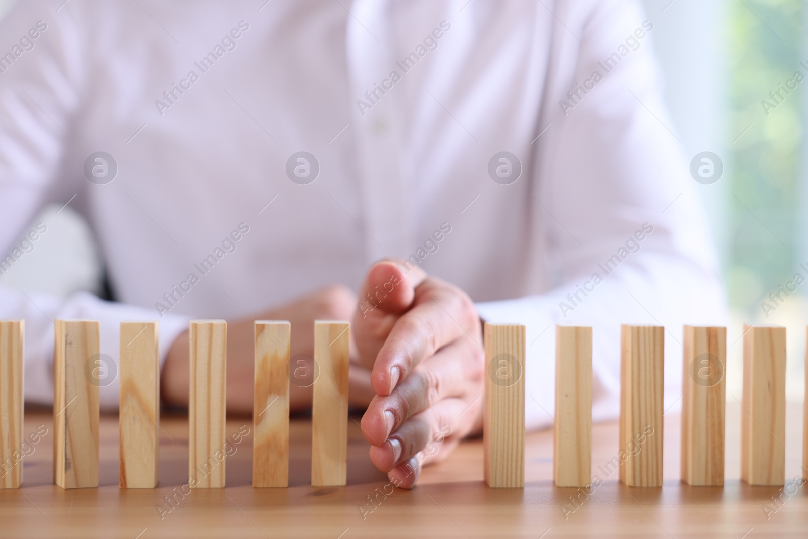 Photo of Risk. Man stopping domino effect at wooden table, closeup