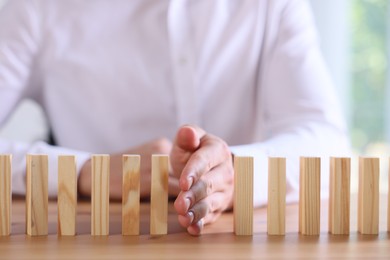 Photo of Risk. Man stopping domino effect at wooden table, closeup