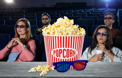 Image of Bucket of fresh popcorn and 3D glasses on table against people watching movie in dark cinema