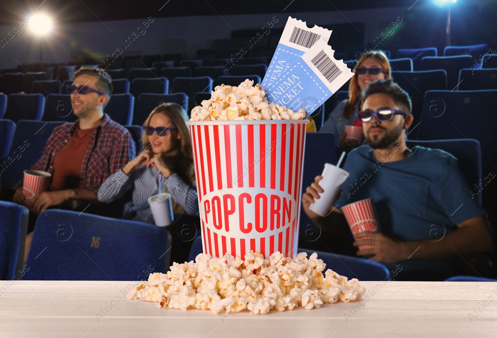 Image of Bucket of fresh popcorn and tickets on table against people watching movie in dark cinema