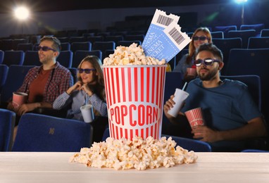 Image of Bucket of fresh popcorn and tickets on table against people watching movie in dark cinema