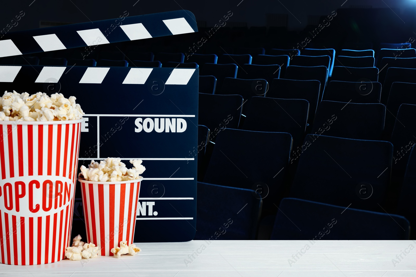 Image of Buckets of fresh popcorn and movie clapper on table in dark cinema