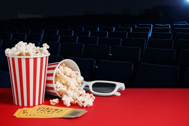 Image of Buckets of fresh popcorn, 3D glasses and cinema tickets on red table in dark movie theater