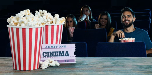 Image of Buckets of fresh popcorn and ticket on table against people watching movie in dark cinema