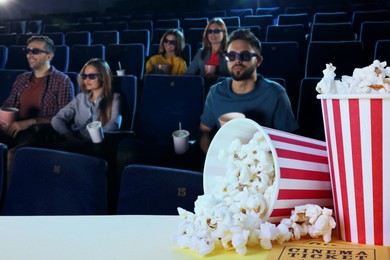 Image of Buckets of fresh popcorn and tickets on table against people watching movie in dark cinema