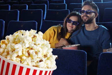 Image of Bucket of fresh popcorn against couple watching movie in dark cinema
