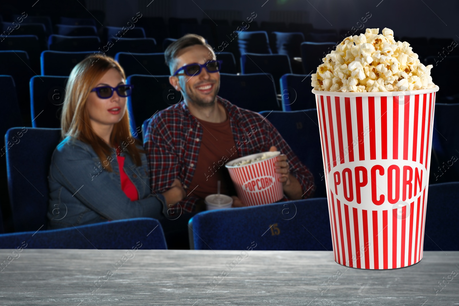 Image of Bucket of fresh popcorn on table against couple watching movie in dark cinema