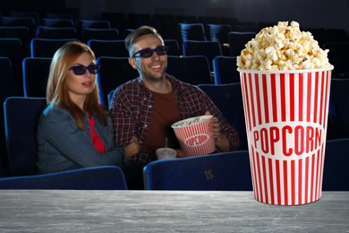 Image of Bucket of fresh popcorn on table against couple watching movie in dark cinema