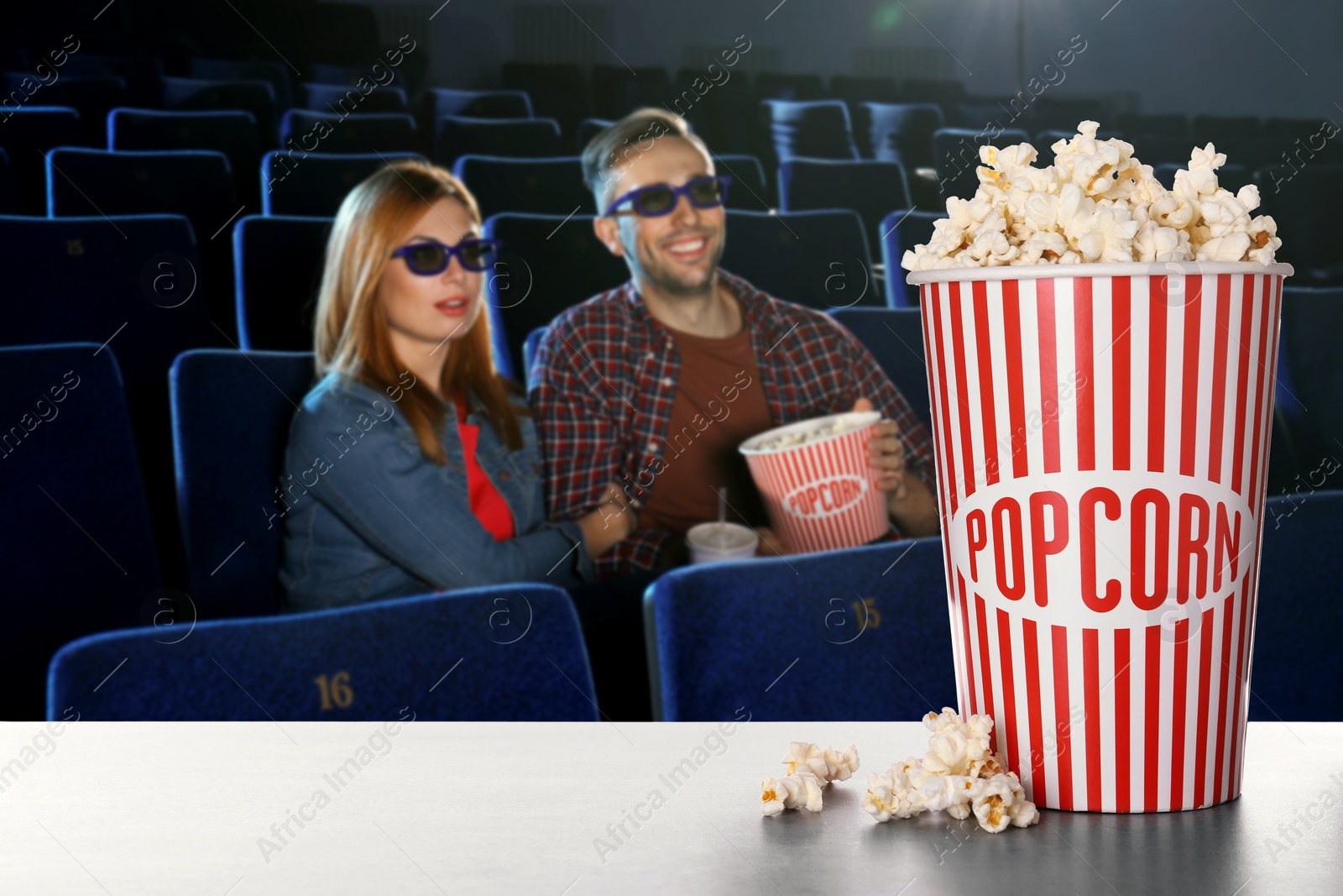 Image of Bucket of fresh popcorn on table against couple watching movie in dark cinema