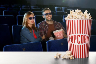 Image of Bucket of fresh popcorn on table against couple watching movie in dark cinema
