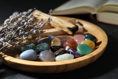 Photo of Different beautiful gemstones, lavender flowers, palo santo and book on black table, closeup