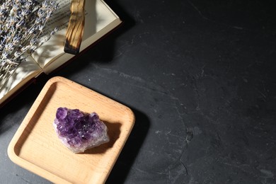 Photo of Beautiful amethyst gemstone, lavender flowers, palo santo and book on black table, above view. Space for text