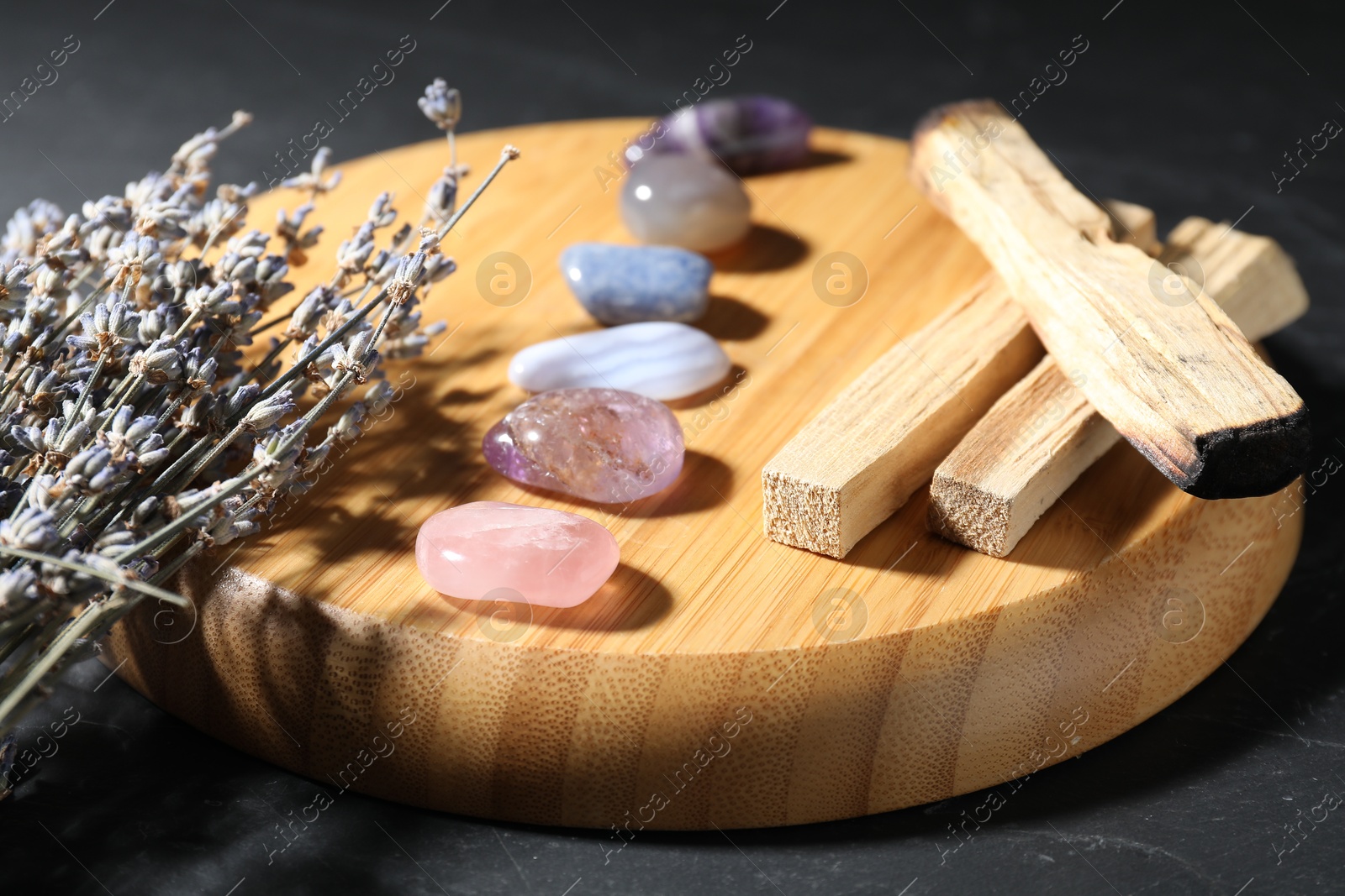 Photo of Different beautiful gemstones, lavender flowers and palo santo on black table, closeup