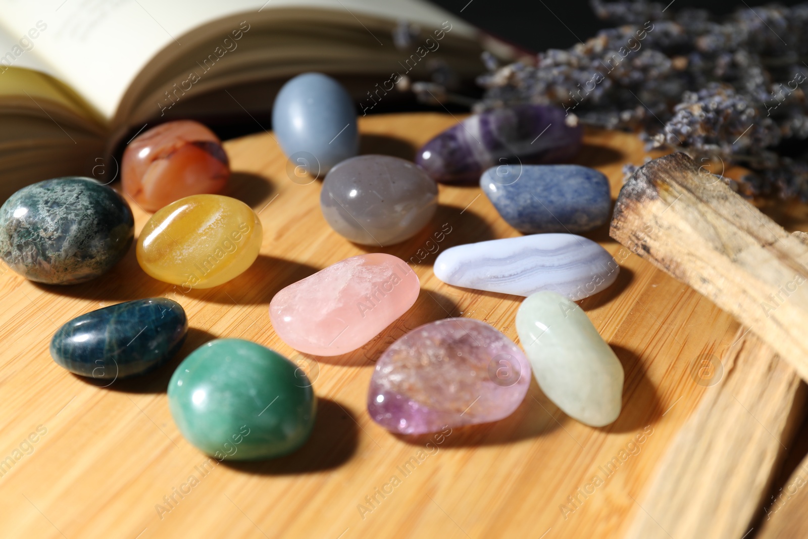 Photo of Different beautiful gemstones, lavender flowers, palo santo and book on table, closeup