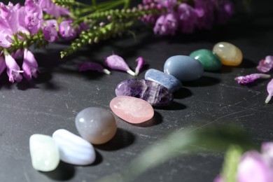 Photo of Different beautiful gemstones and flowers on black table, closeup