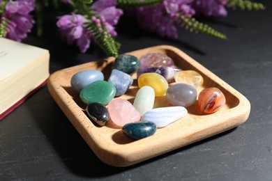 Photo of Different beautiful gemstones, book and flowers on black table, closeup