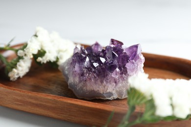 Photo of Beautiful amethyst gemstone and flowers on table, closeup