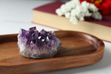 Photo of Beautiful amethyst gemstone, book and flowers on white table, closeup