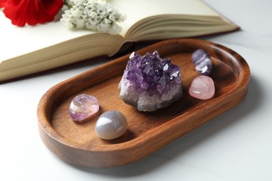 Photo of Different beautiful gemstones, book and flowers on white marble table, closeup