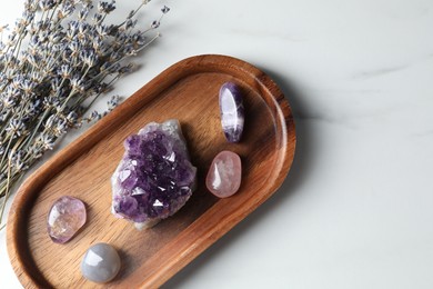Photo of Different beautiful gemstones and lavender flowers on white marble table, flat lay. Space for text