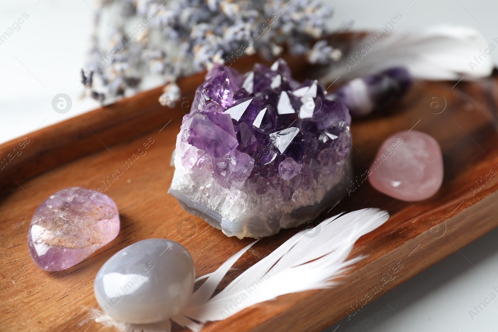 Photo of Different beautiful gemstones, feather and lavender flowers on white table, closeup