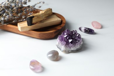 Photo of Different beautiful gemstones, palo santo and lavender flowers on white table, closeup