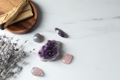 Photo of Different beautiful gemstones, palo santo and lavender flowers on white marble table, flat lay. Space for text