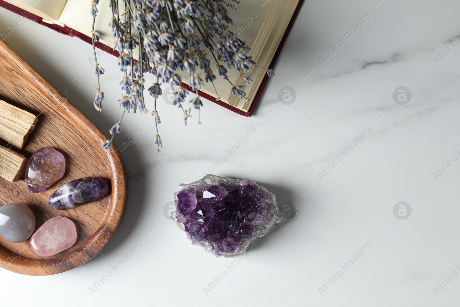 Photo of Different beautiful gemstones, book and lavender flowers on white marble table, flat lay. Space for text