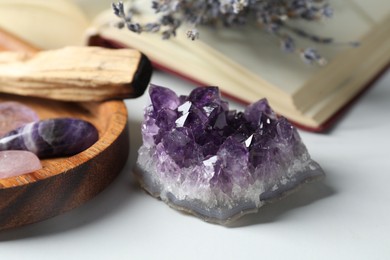 Photo of Different beautiful gemstones, palo santo, book and lavender flowers on white table, closeup