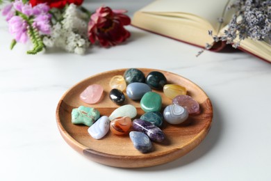 Photo of Different beautiful gemstones, book and flowers on white marble table, closeup