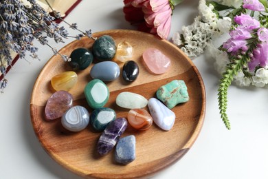 Photo of Different beautiful gemstones, flowers and book on white table, above view