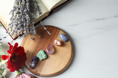 Photo of Different beautiful gemstones, book and flowers on white marble table, flat lay. Space for text