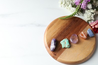 Photo of Different beautiful gemstones and flowers on white marble table, flat lay. Space for text