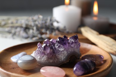 Photo of Different beautiful gemstones, palo santo, lavender flowers and burning candles on table, closeup