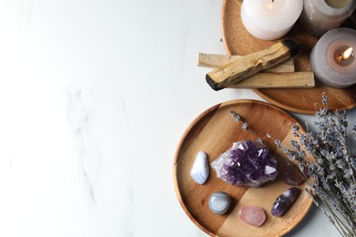 Photo of Different beautiful gemstones, palo santo, lavender and burning candles on white marble table, flat lay. Space for text