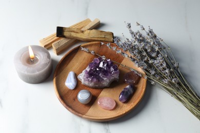 Photo of Different beautiful gemstones, palo santo, lavender flowers and burning candle on white marble table, above view