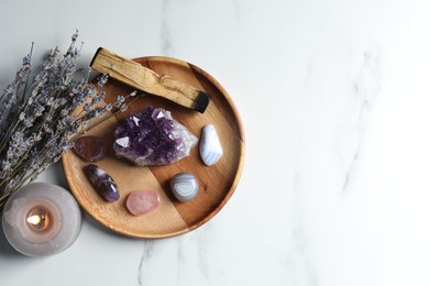 Photo of Different beautiful gemstones, palo santo, lavender flowers and burning candle on white marble table, flat lay. Space for text