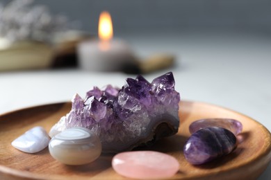 Photo of Different beautiful gemstones and burning candle on table, closeup