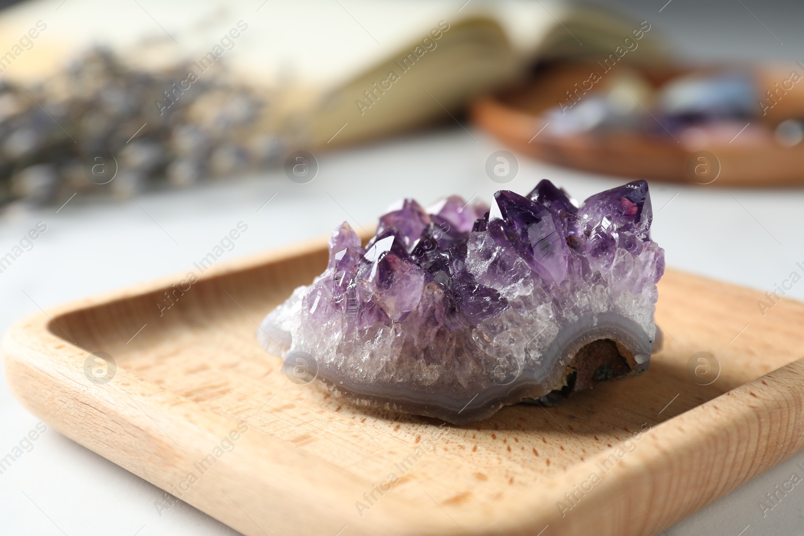 Photo of Beautiful amethyst gemstone, book and flowers on table, closeup