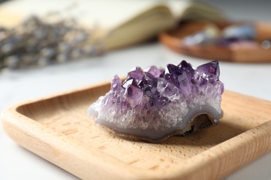 Photo of Beautiful amethyst gemstone, book and flowers on table, closeup