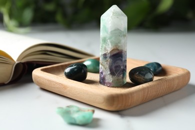 Photo of Different beautiful gemstones and book on white marble table, closeup