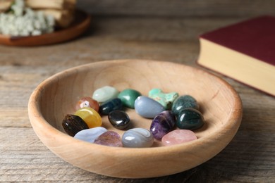 Photo of Different beautiful gemstones and book on wooden table, closeup