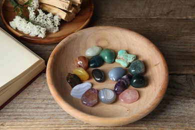 Photo of Different beautiful gemstones, flowers, palo santo and book on wooden table, closeup