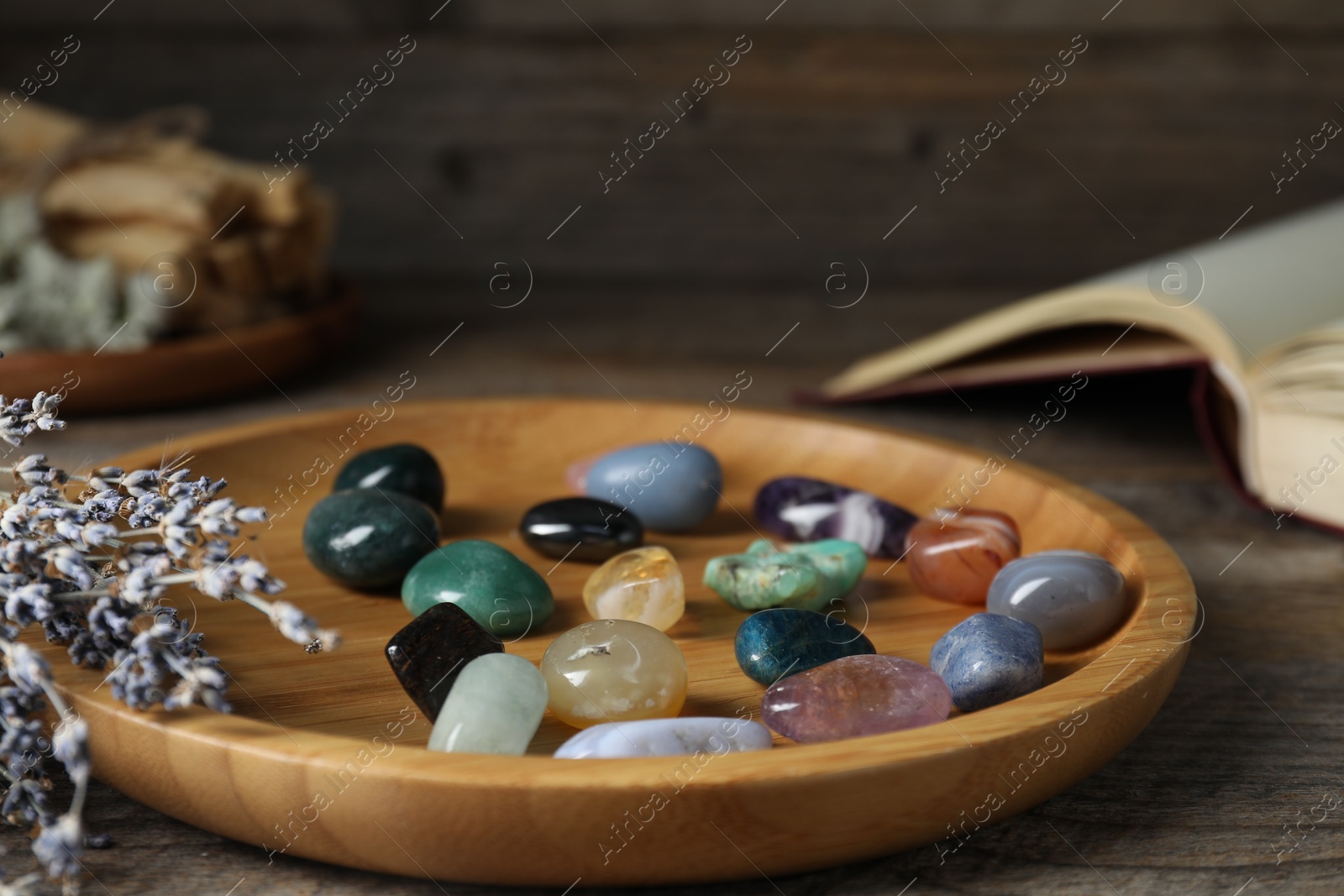 Photo of Different beautiful gemstones, lavender flowers and book on wooden table, closeup