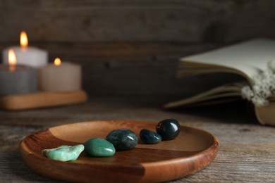Photo of Different beautiful gemstones, burning candles, flowers and book on wooden table, closeup