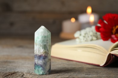 Photo of Beautiful fluorite gemstone, book, flowers and burning candles on wooden table, closeup