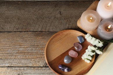 Photo of Different beautiful gemstones, burning candles, flowers and book on wooden table, flat lay. Space for text