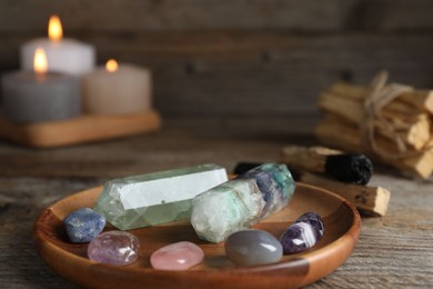 Photo of Different beautiful gemstones, palo santo and burning candles on wooden table, closeup