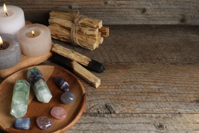 Photo of Different beautiful gemstones, palo santo and burning candles on wooden table, closeup. Space for text